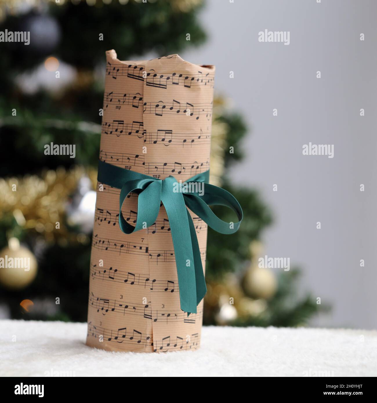 Hermoso regalo de Navidad decorado con música y notas de papel temático y cinta verde satinada. El presente fue fotografiado con un árbol de Navidad. Foto de stock