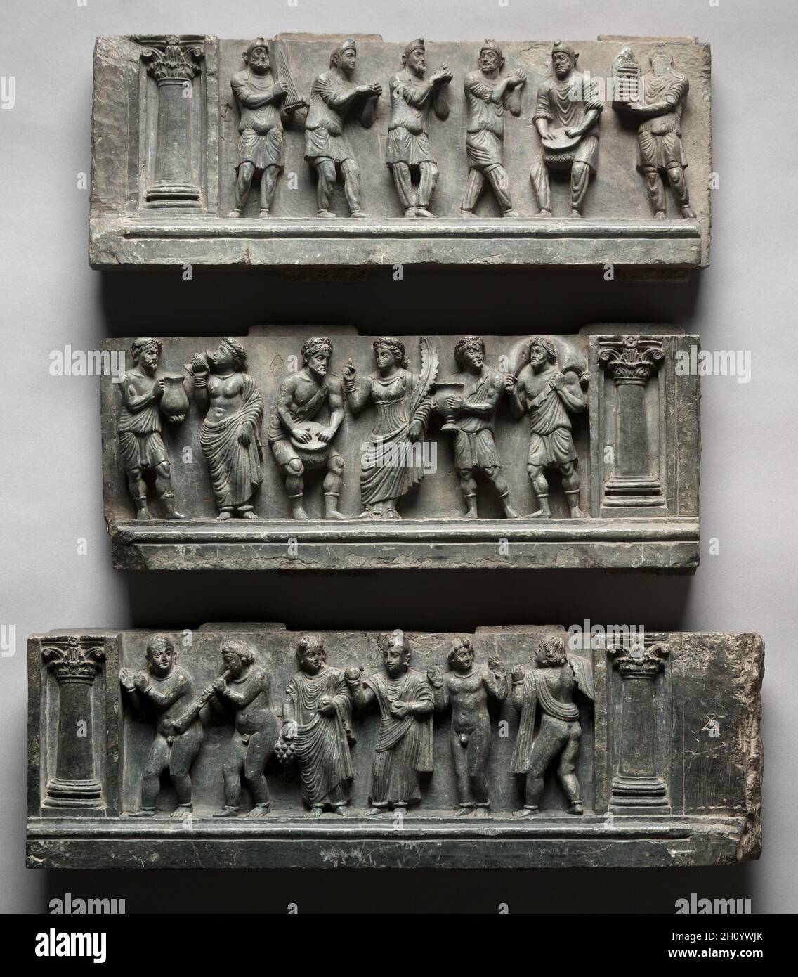 Alivio de Bacchanalian, AD 1-100. Pakistán, Gandhara, zona de Buner, período temprano de Kushan (1–320 dC). Esquisto; total: 49,6 x 150,5 cm (19 1/2 x 59 1/4 pulg.); primera sección: 17,1 x 44,5 cm (6 3/4 x 17 1/2 pulg.); segunda sección: 16,5 x 53 cm (6 1/2 x 20 7/8 pulg.); tercera sección: 16 x 53 cm (6 5/16 x 20 7/8 pulg.). Los phrygians con sus pantalones, túnicas, y gorras cónicas juegan música, danza, y clap, mientras que las figuras griegas beben de tazas acanaladas llenas de vino decantadas de lanzadores llenos de una piel de vino, mostrado hetted en los hombros de la figura a la derecha. La diversidad multicultural de la región bec Foto de stock