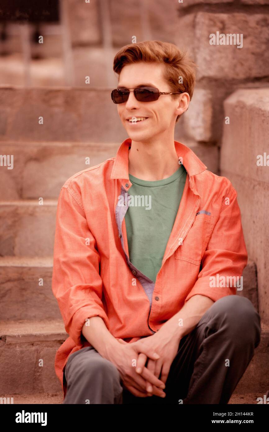 Un hombre joven guapo con camisa naranja en la ciudad, sentado en la  escalera Fotografía de stock - Alamy