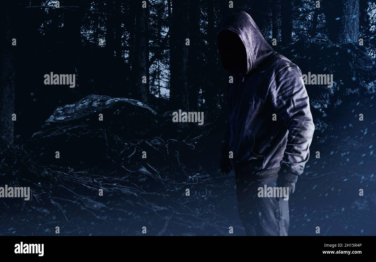 Foto de terror extraño hombre acosador en la capucha negra y ropa sobre el fondo del bosque. Foto de stock