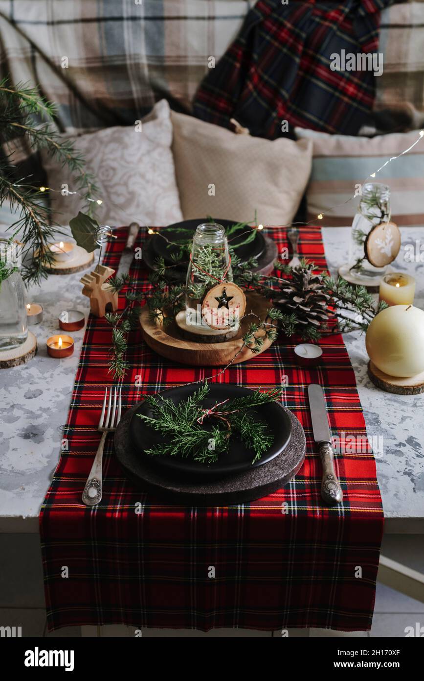Mesa de Navidad con corona en el plato, adornos decorativos de madera y  manteles de cuadros rojos con luces amarillas en el fondo Fotografía de  stock - Alamy