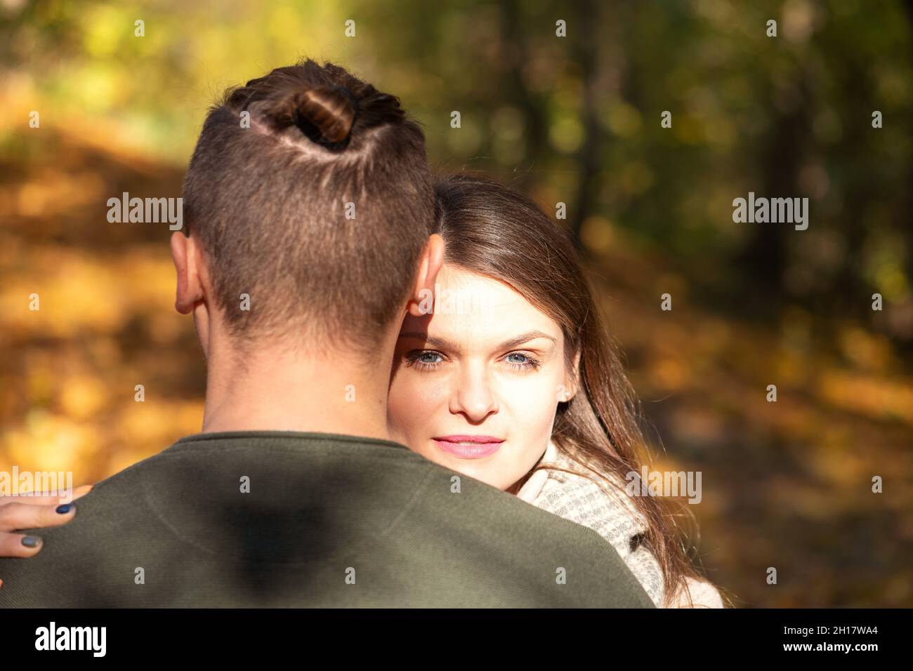 Amor, ocio, naturaleza, concepto de relación. Hermosa mujer morena con lápiz labial rosa y rostro iluminado por la luz del sol abrazando al hombre en otoño amarillo Foto de stock