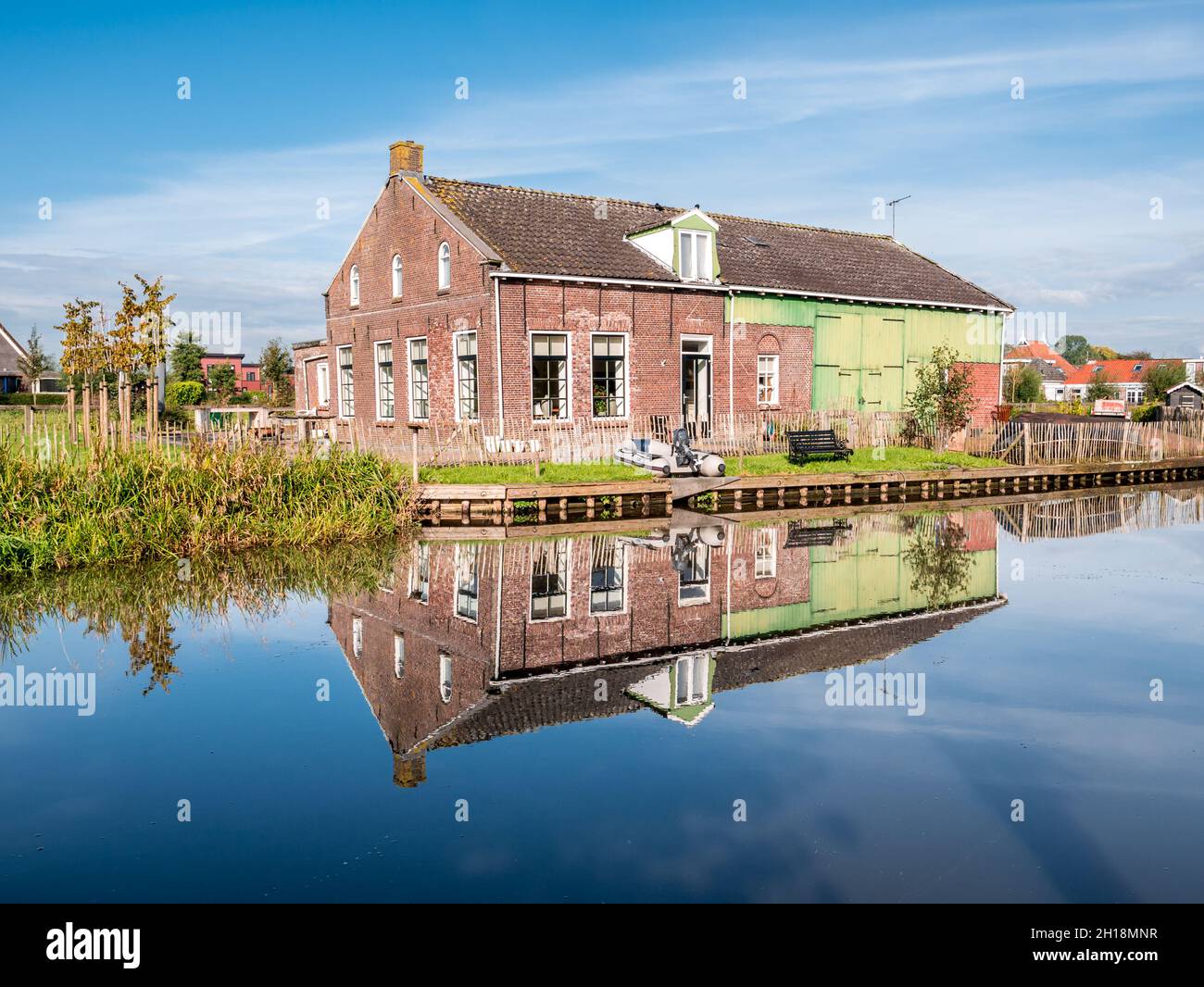 Casa y granero que se refleja en el agua de Wargaastervaart en el pueblo de Wergea, Leeuwarden, Friesland, Países Bajos Foto de stock
