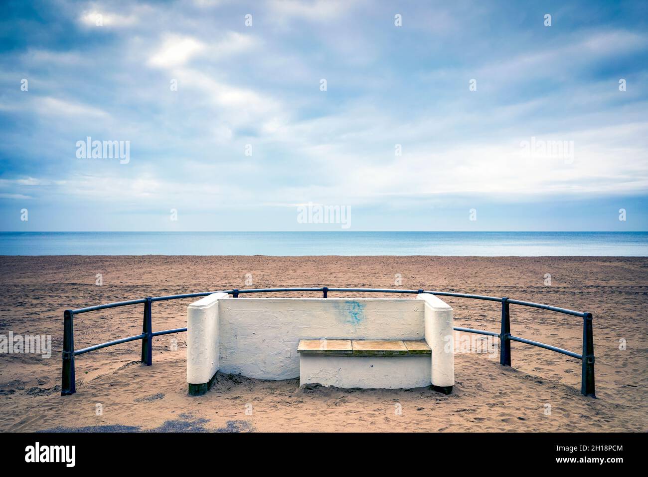 Playa de arena desierta con asiento y barandillas en primer plano Foto de stock