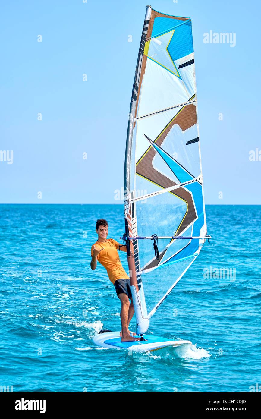 un chico se monta en una tabla con una vela Foto de stock