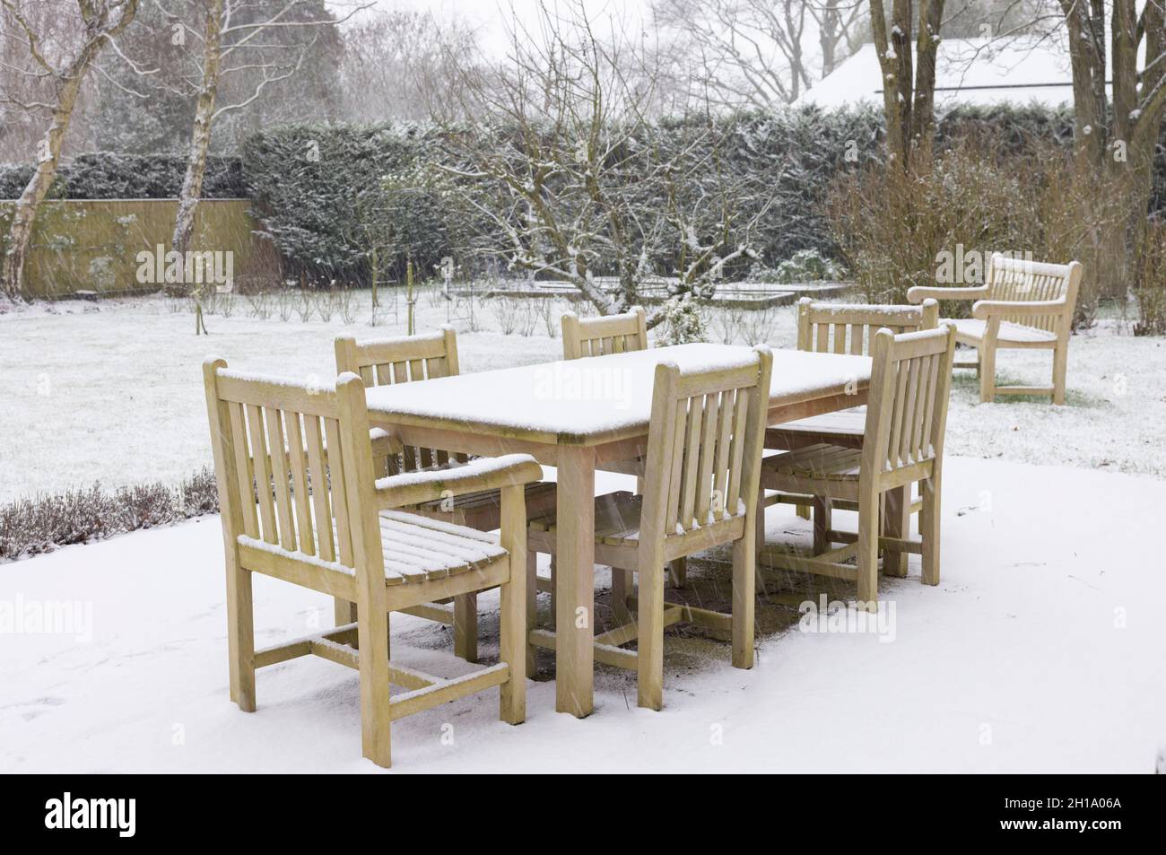 Patio jardín con mesas y sillas, mesa de madera y sillas cubiertas de nieve en invierno, Reino Unido Foto de stock