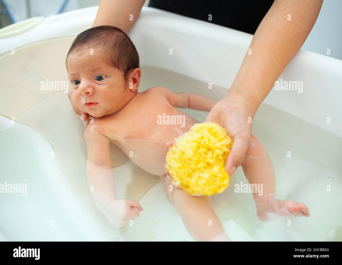 Primer baño de bebé recién nacido. La madre lava al bebé con una esponja natural. Foto de stock