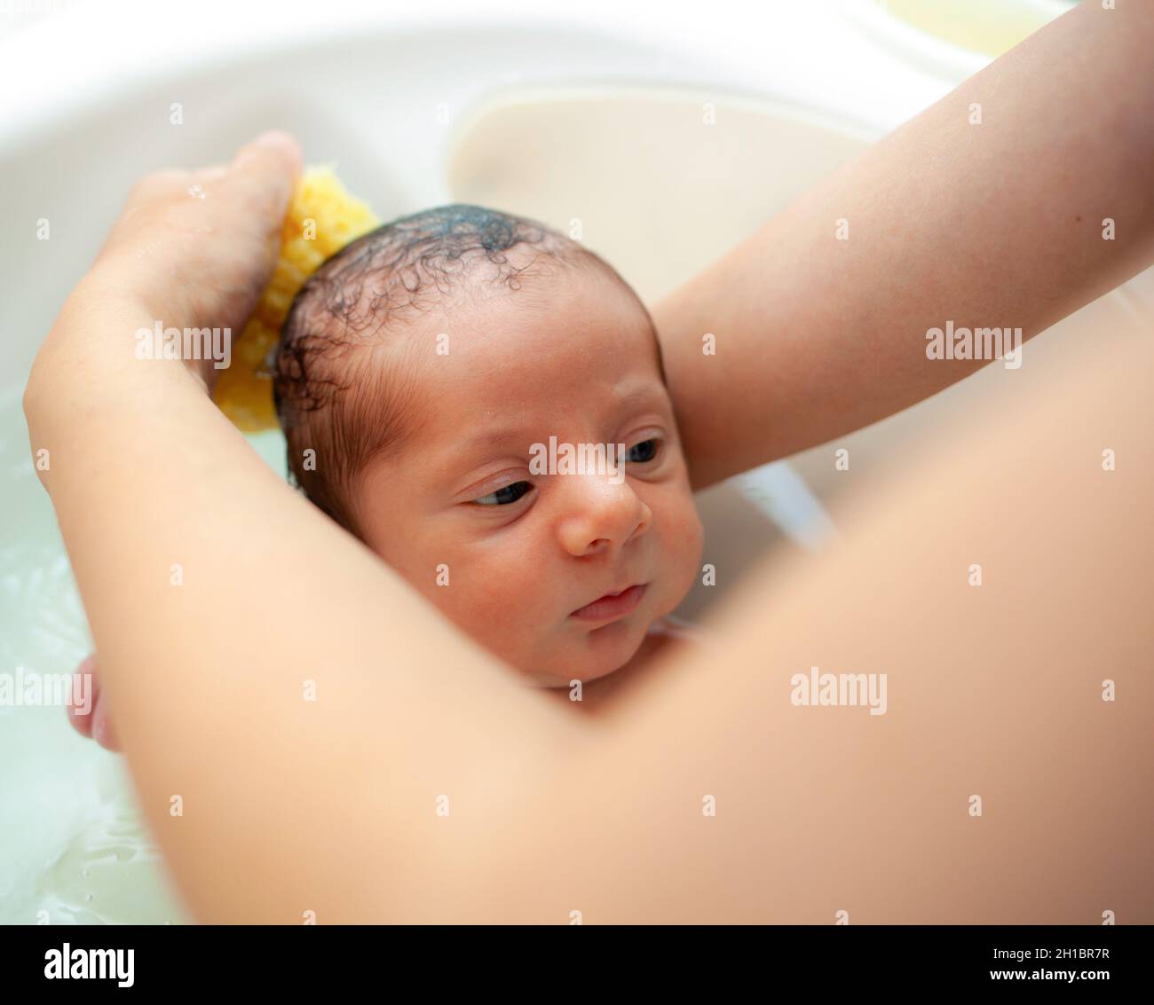 Primer baño de bebé recién nacido. La madre lava al bebé con una esponja natural. Foto de stock