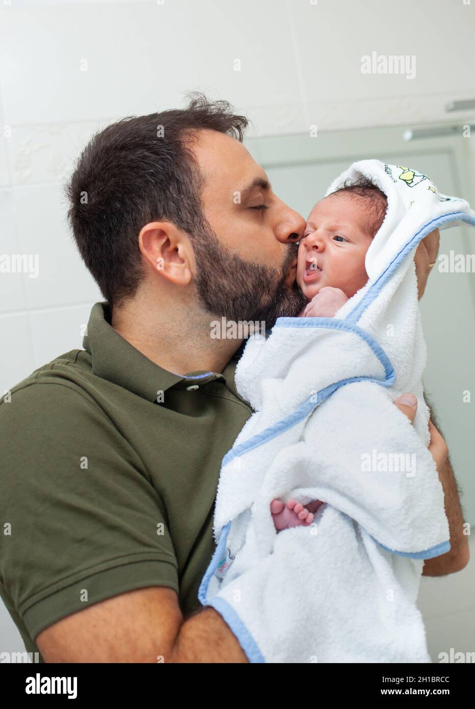 Primer baño de bebé recién nacido. El bebé está en el albornoz en los brazos de su padre. Foto de stock