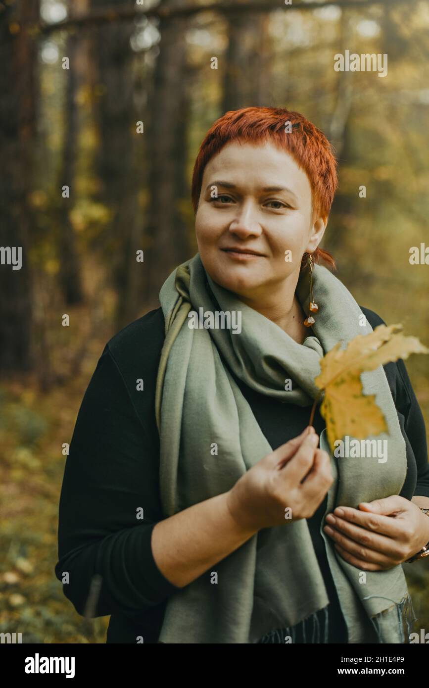Sonriente mujer de mediana edad de 30-40 años camina por el bosque de otoño Foto de stock