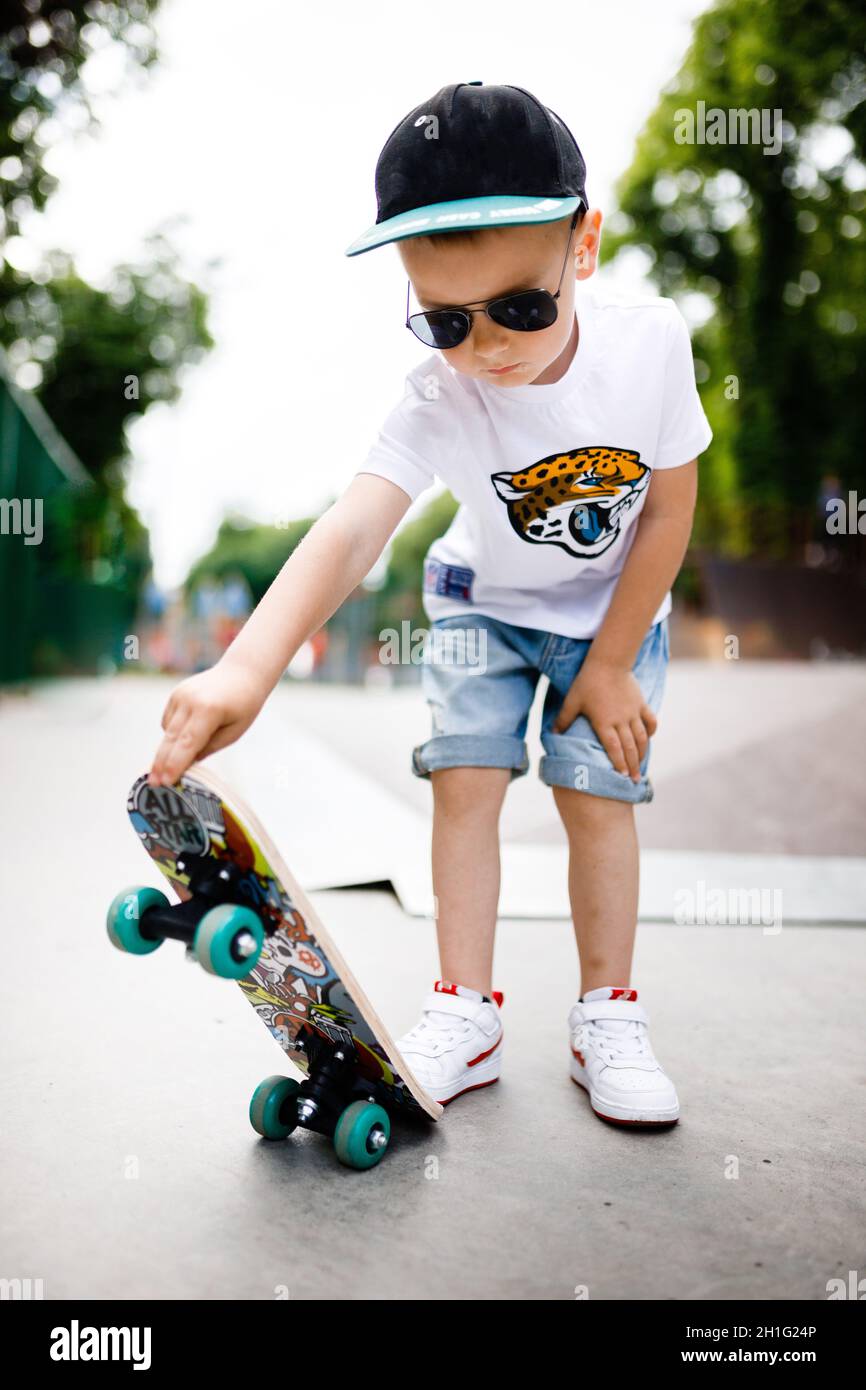 Niño con un skate en un parque de skate. Un niño con gafas aprende a  patinar con ropa elegante. Un poco extremo Fotografía de stock - Alamy