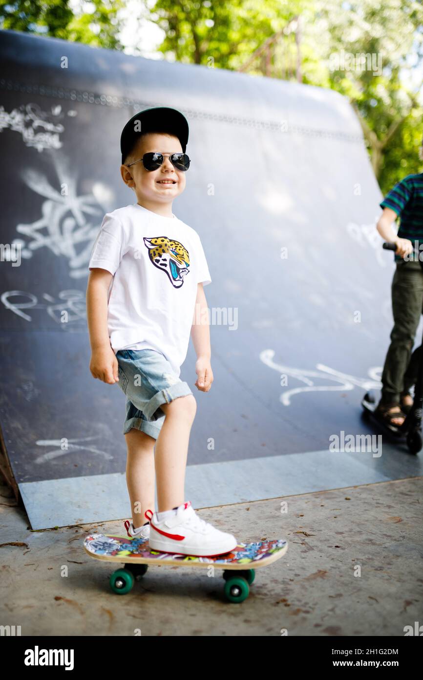 Niño con un skate en un parque de skate. Un niño con gafas aprende a  patinar con ropa elegante. Un poco extremo Fotografía de stock - Alamy