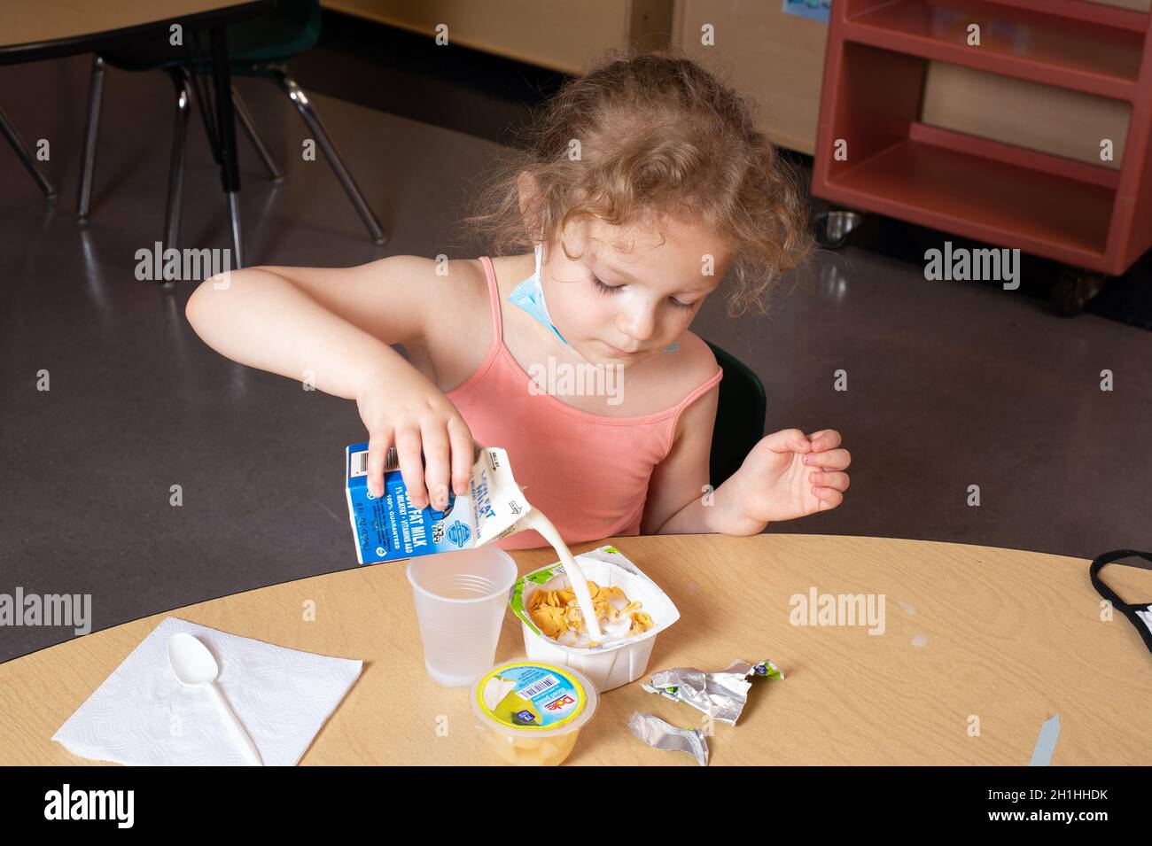 Educación Preescolar niña de 4-5 años que vierte su propia leche en su cereal durante el desayuno Foto de stock