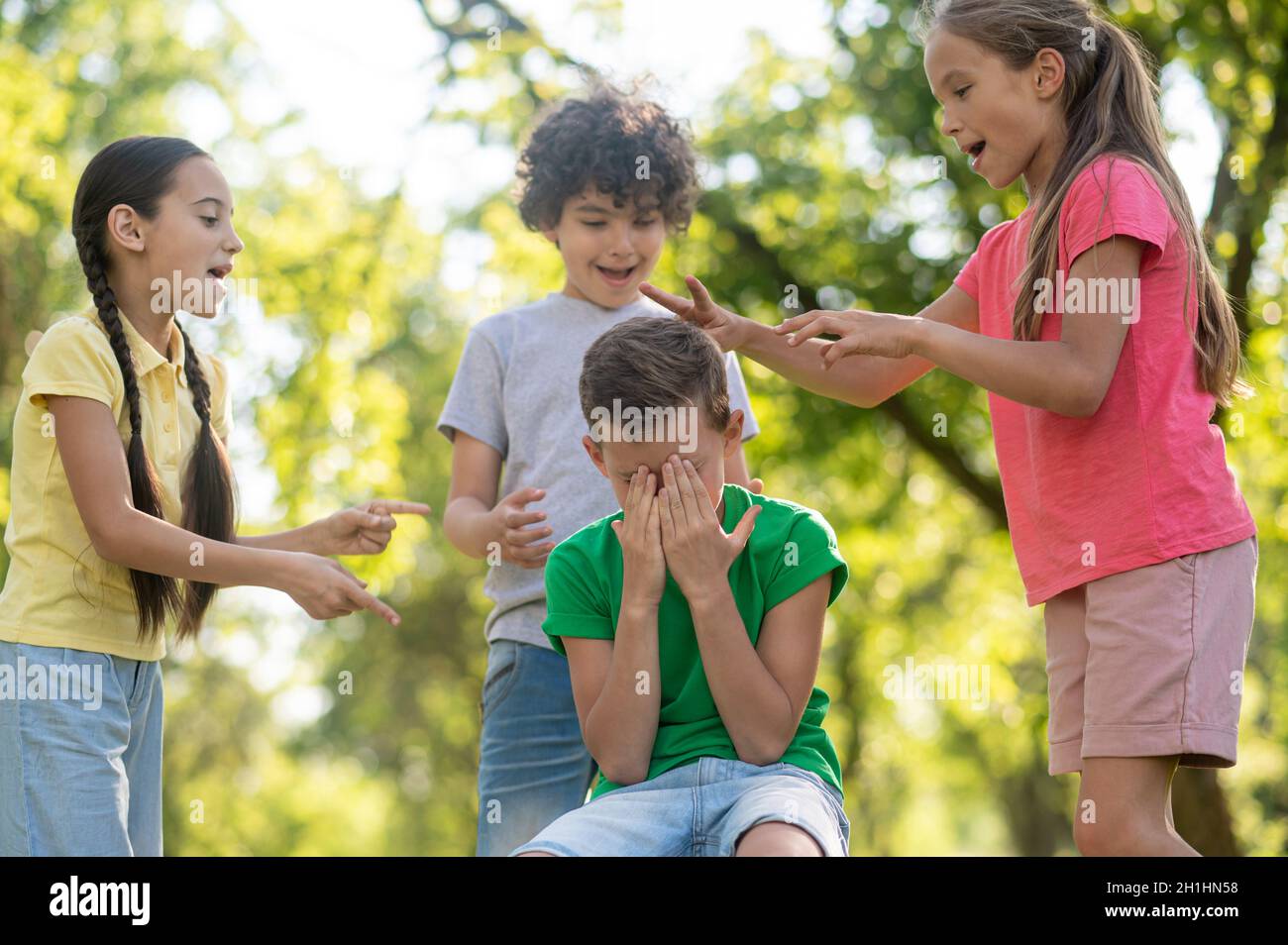 Niños que ofenden al niño que cubre la cara con las manos. Foto de stock