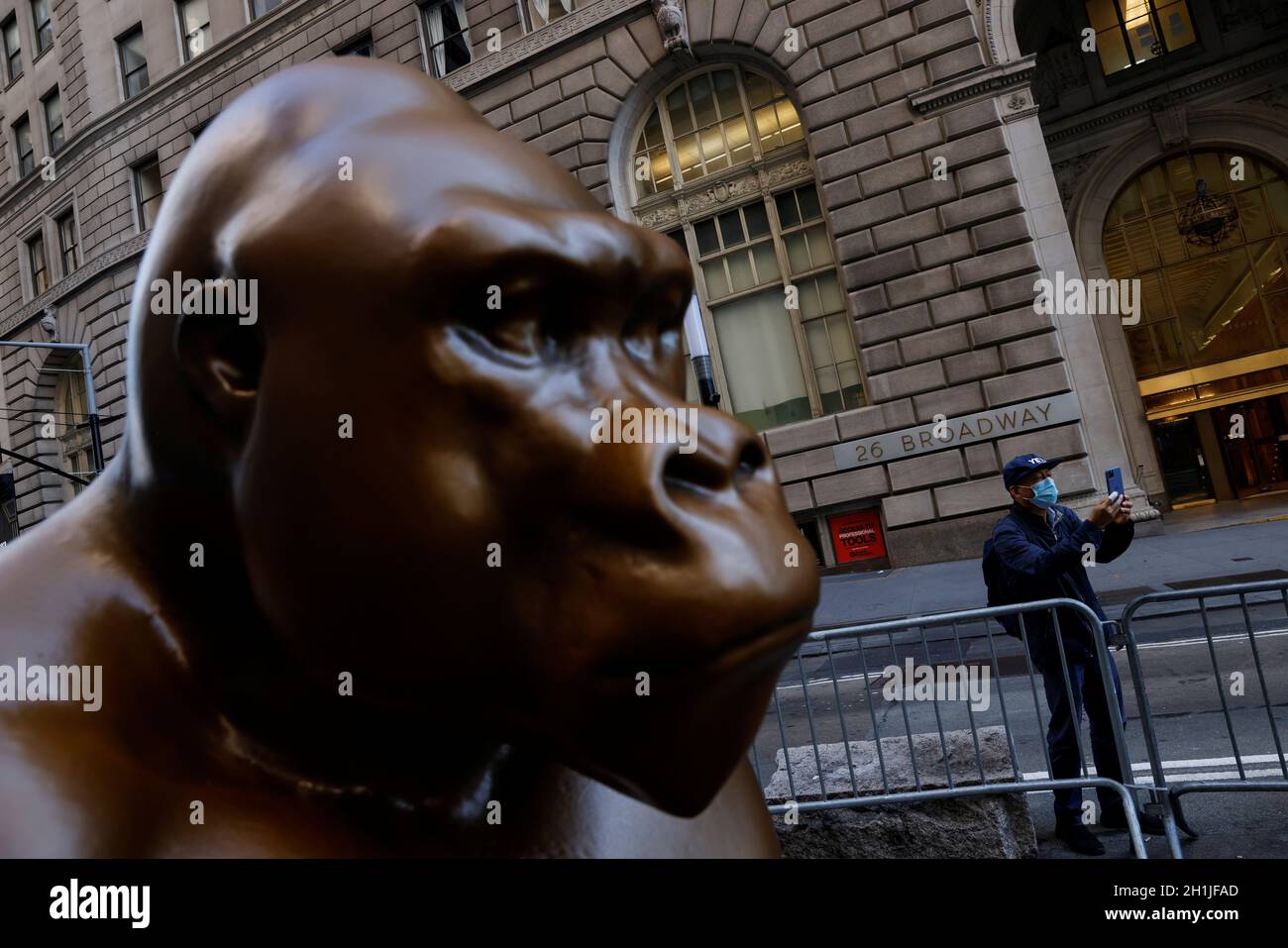 Un hombre toma una foto con una máscara protectora cerca de la estatua de la gorila de Harambe, encargada por los fundadores de Sapien.Network Ankit Bhatia y Rob Giometti, frente a la estatua de Charging Bull, también conocida como el Wall St. Bull, en Bowling Green Park en la ciudad de Nueva York, Nueva York, EE.UU., 18 de octubre de 2021. REUTERS/Shannon Stapleton Foto de stock