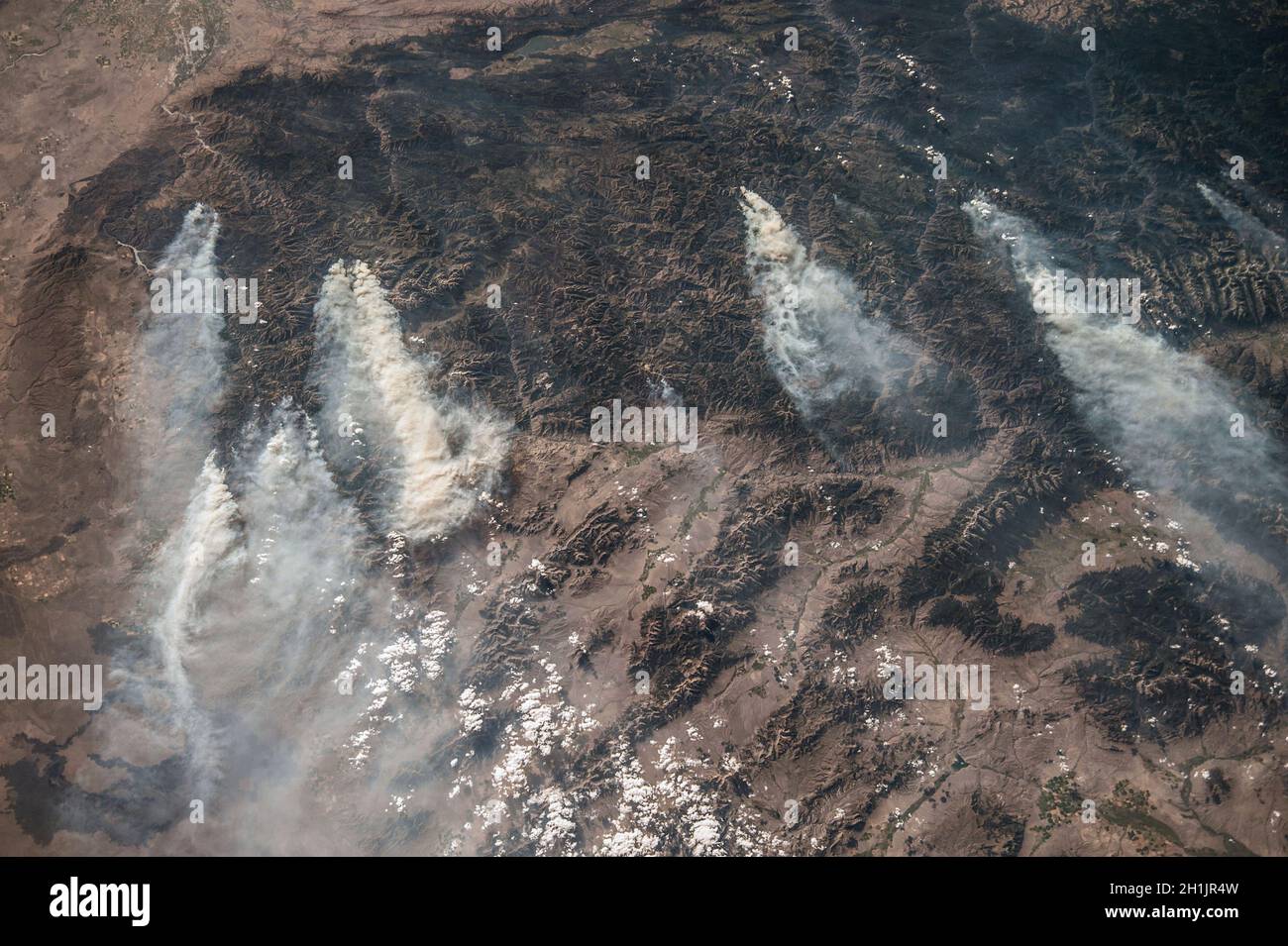 La Tierra vista desde la Estación Espacial Internacional: Idaho, Estados Unidos. Agosto de 2013. Las zonas oscuras son todas montañas boscosas. Dentro de esta región montañosa, se pueden observar varios incendios que producen extensos penachos de humo, la mayoría de ellos provocados por un rayo. Esta imagen muestra el patrón común de vientos occidentales que transportan humo en dirección este. Una versión optimizada y mejorada de una imagen de NASA / crédito de la NASA. Foto de stock