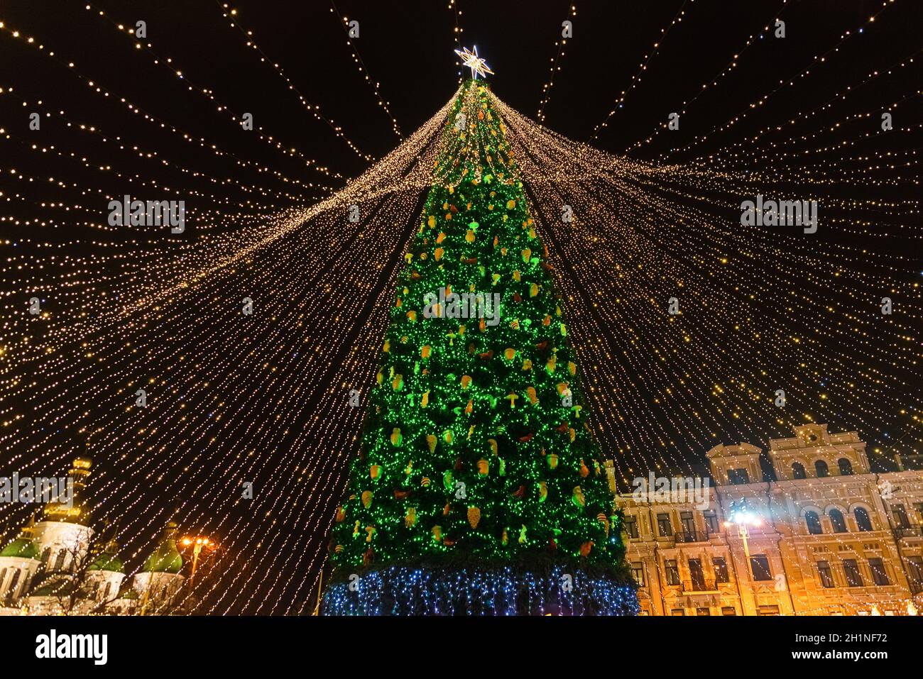 Un árbol de Navidad grande, brillante y brillante, decorado con guirnaldas,  juguetes y luces de colores, se encuentra en la plaza central en medio del  año Nuevo ho Fotografía de stock -