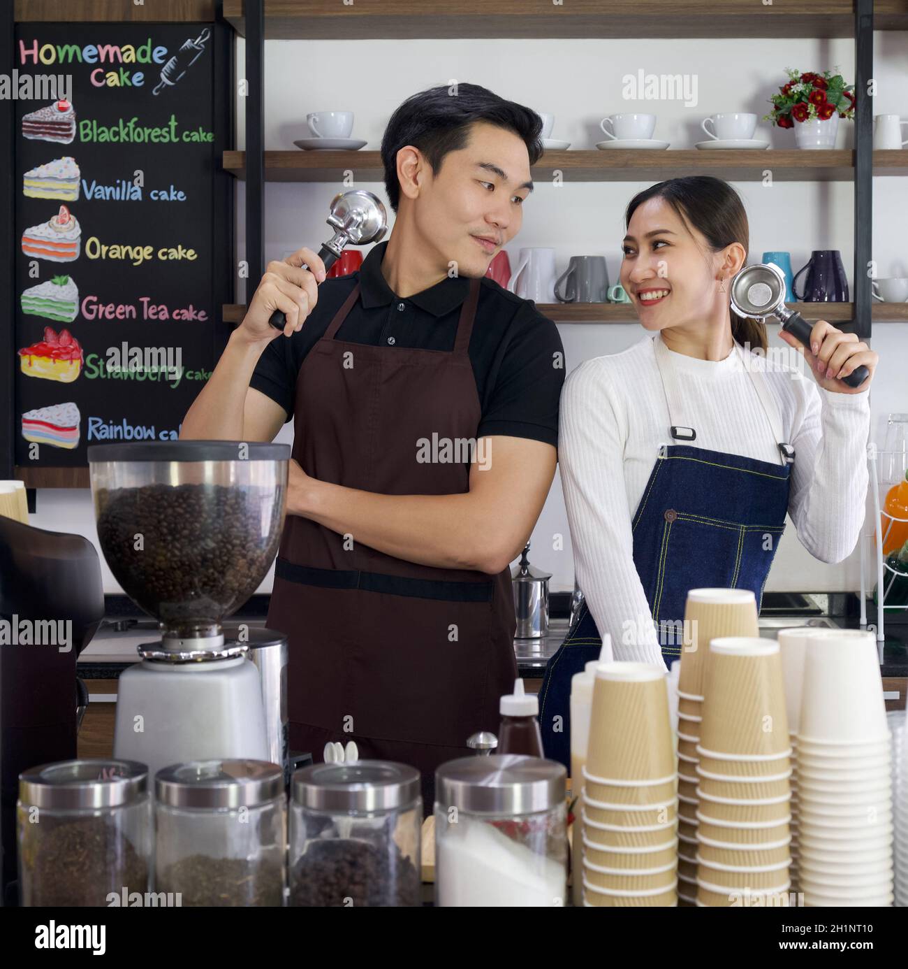 El tendero y el barista que sostiene Espresso Machine Portafters con una sonrisa. Ambiente matutino en una cafetería. Foto de stock