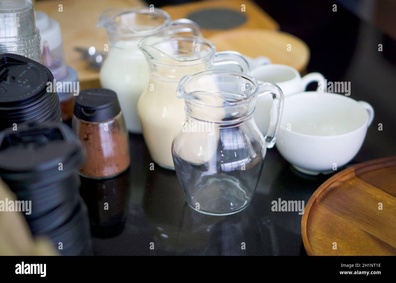 Varios componentes esenciales para hacer café se colocan en la encimera de granito. Leche fresca, leche condensada, Cacao en polvo. Foto de stock