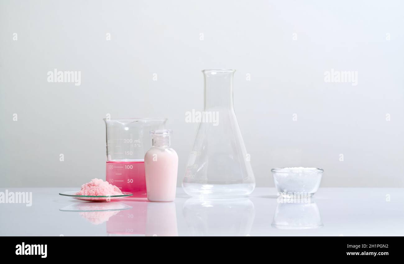 Crema para el cuidado de la belleza, químicos de copos rosados, permanganato potásico líquido y cera de ésteres cetílicos sobre mesa blanca de laboratorio. Foto de stock