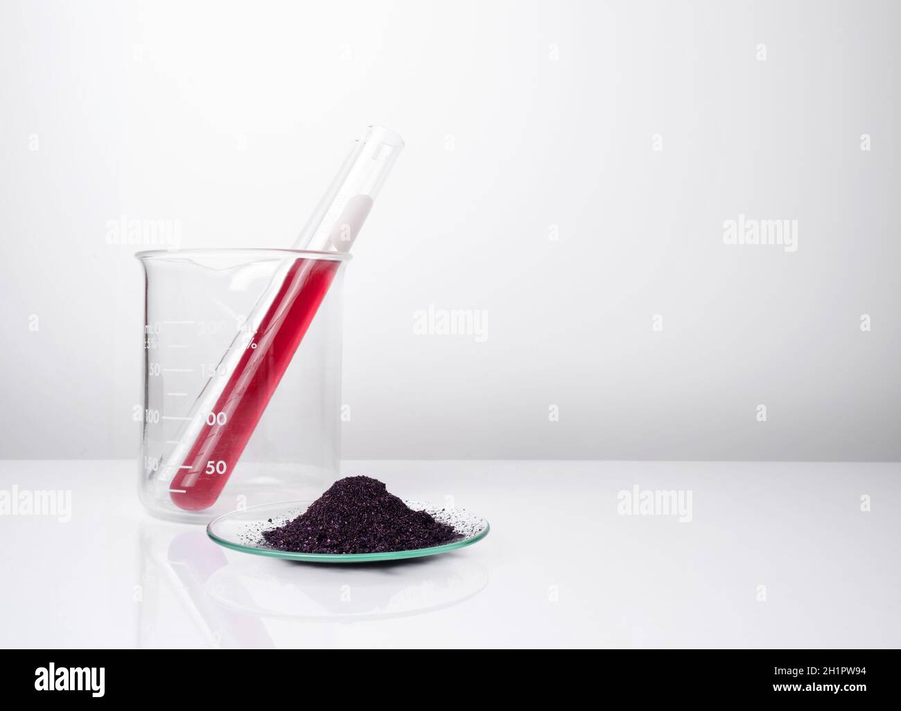 Permanganato potásico líquido en el tubo de ensayo colocar junto a KMnO4 en el vidrio químico de reloj. Ingredientes químicos cosméticos sobre mesa blanca de laboratorio. Foto de stock