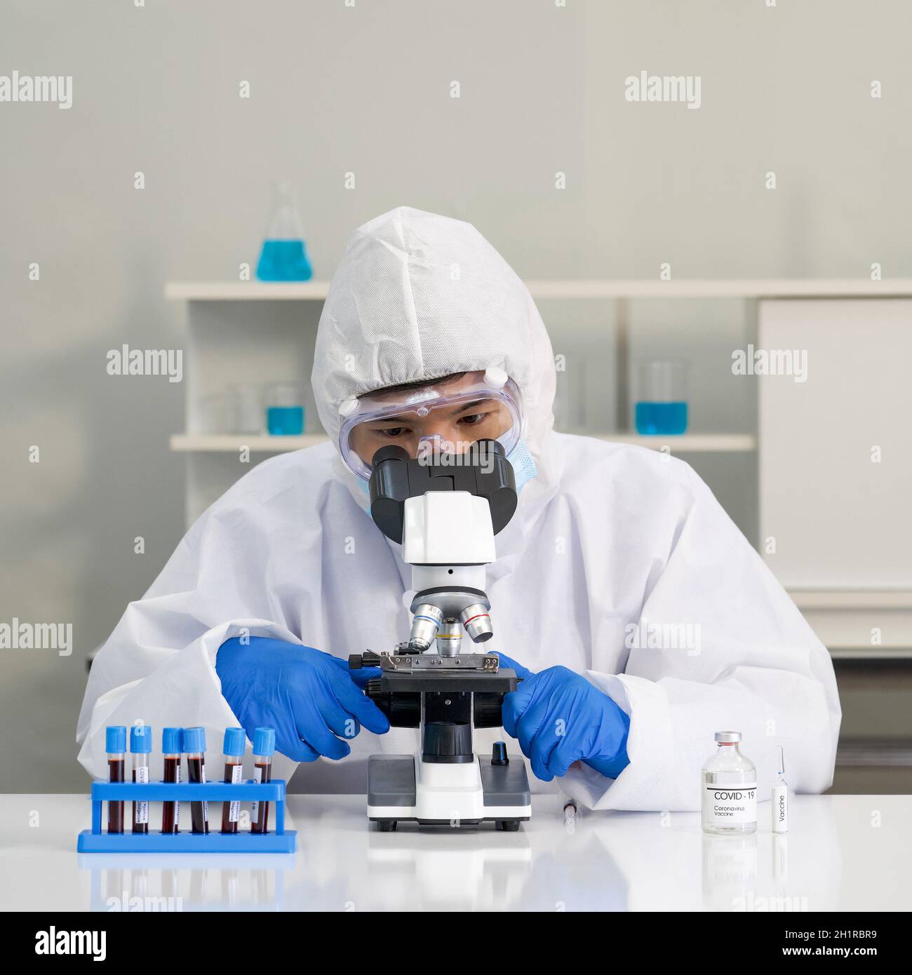 Investigador epidemiológico en la ropa protectora del virus Utilice un microscopio para observar la muestra de sangre de las personas infectadas. Enfermedad de coronavirus 2019 (COVID-19) Foto de stock