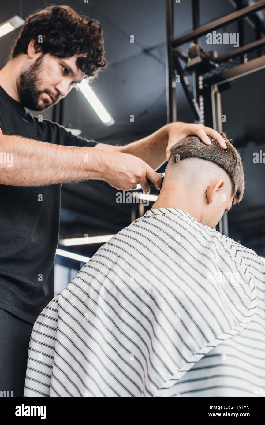 Corte de pelo profesional para hombre y peluquería en una peluquería o  peluquería. Una guapo barbero alto morena le da una maquinilla de afeitar  eléctrica para cortar el pelo a un adolescente