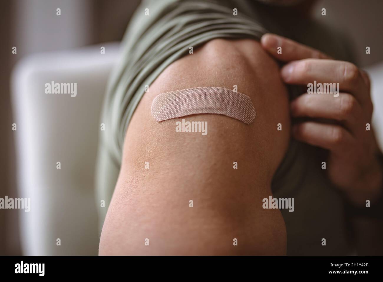 Sección media del hombre caucásico mostrando su hombro vacunado en casa Foto de stock