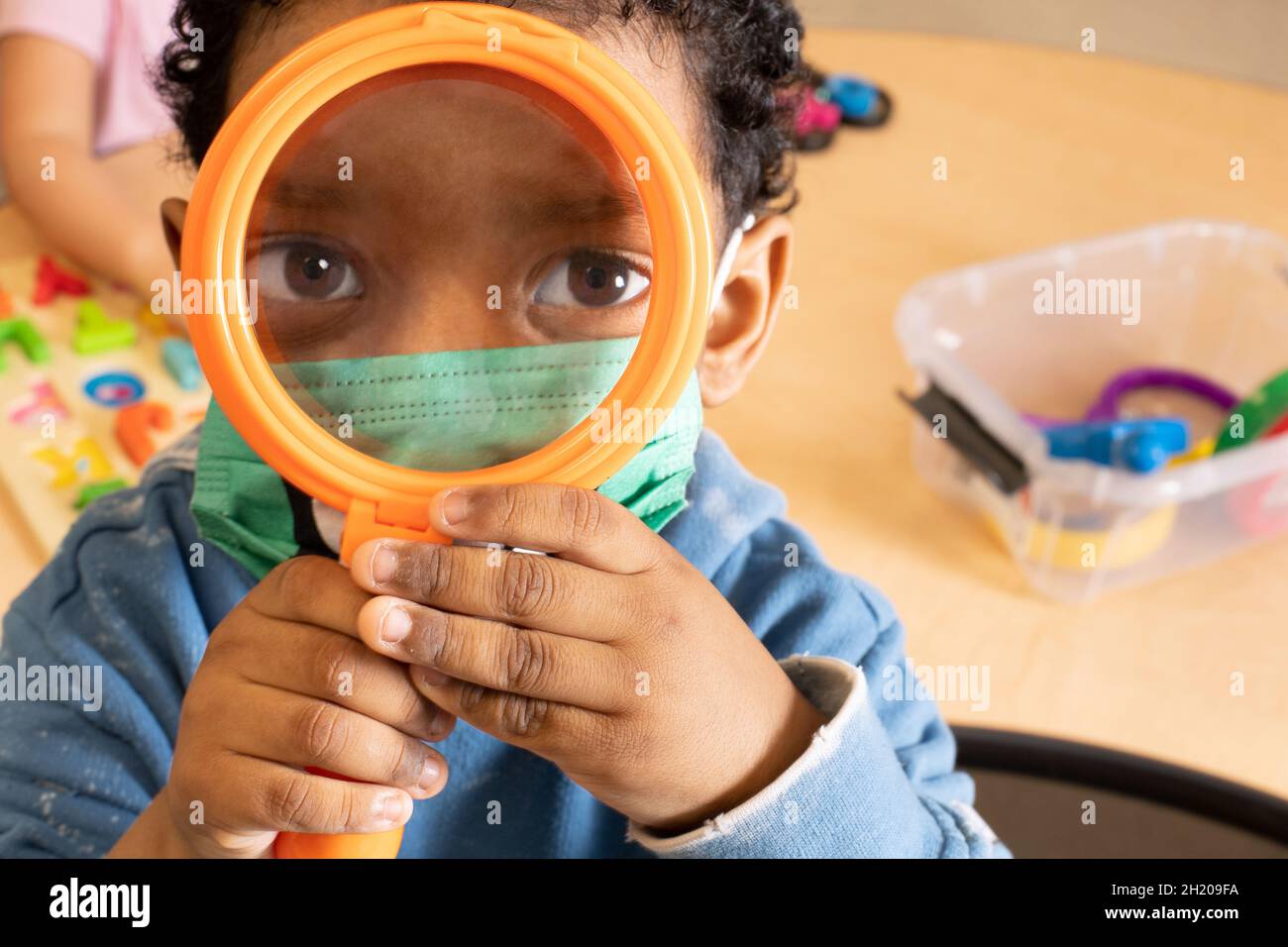 Educación Preescolar Niños de 3-4 años sosteniendo una lupa hasta su cara,  mirando al espectador, usando una máscara facial para protegerse contra  Covid-19 Fotografía de stock - Alamy
