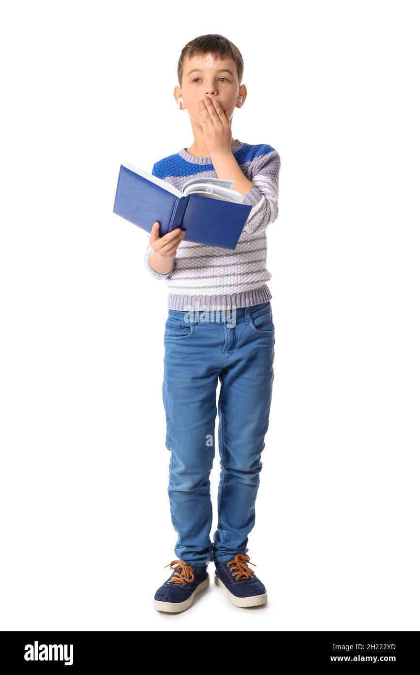 Chico pequeño aburrido con libro y auriculares sobre fondo blanco Foto de stock