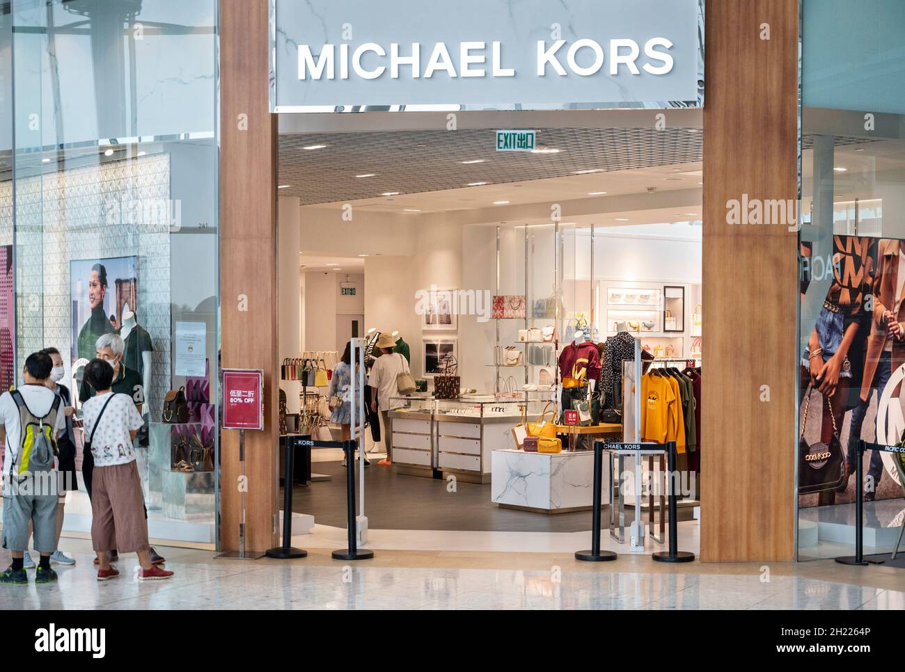 Los compradores se encuentran fuera del logotipo de la tienda de moda de  ropa estadounidense Michael Kors (MK) y se almacenan en el distrito de Tung  Chung en Hong Kong Fotografía de