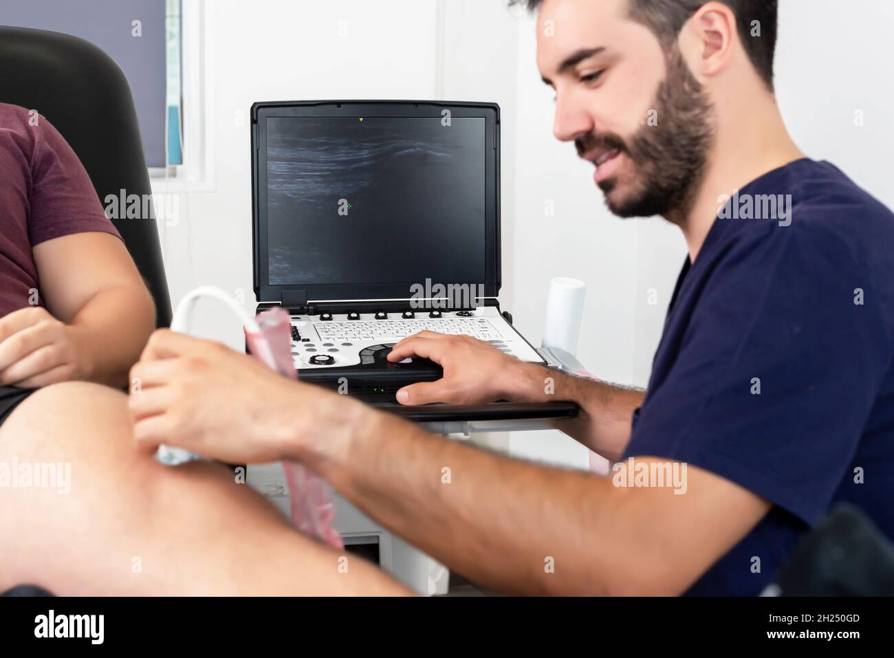 Fisioterapeuta que realiza una ecografía de la rodilla en un paciente tumbado en la camilla. Enfoque selectivo Foto de stock
