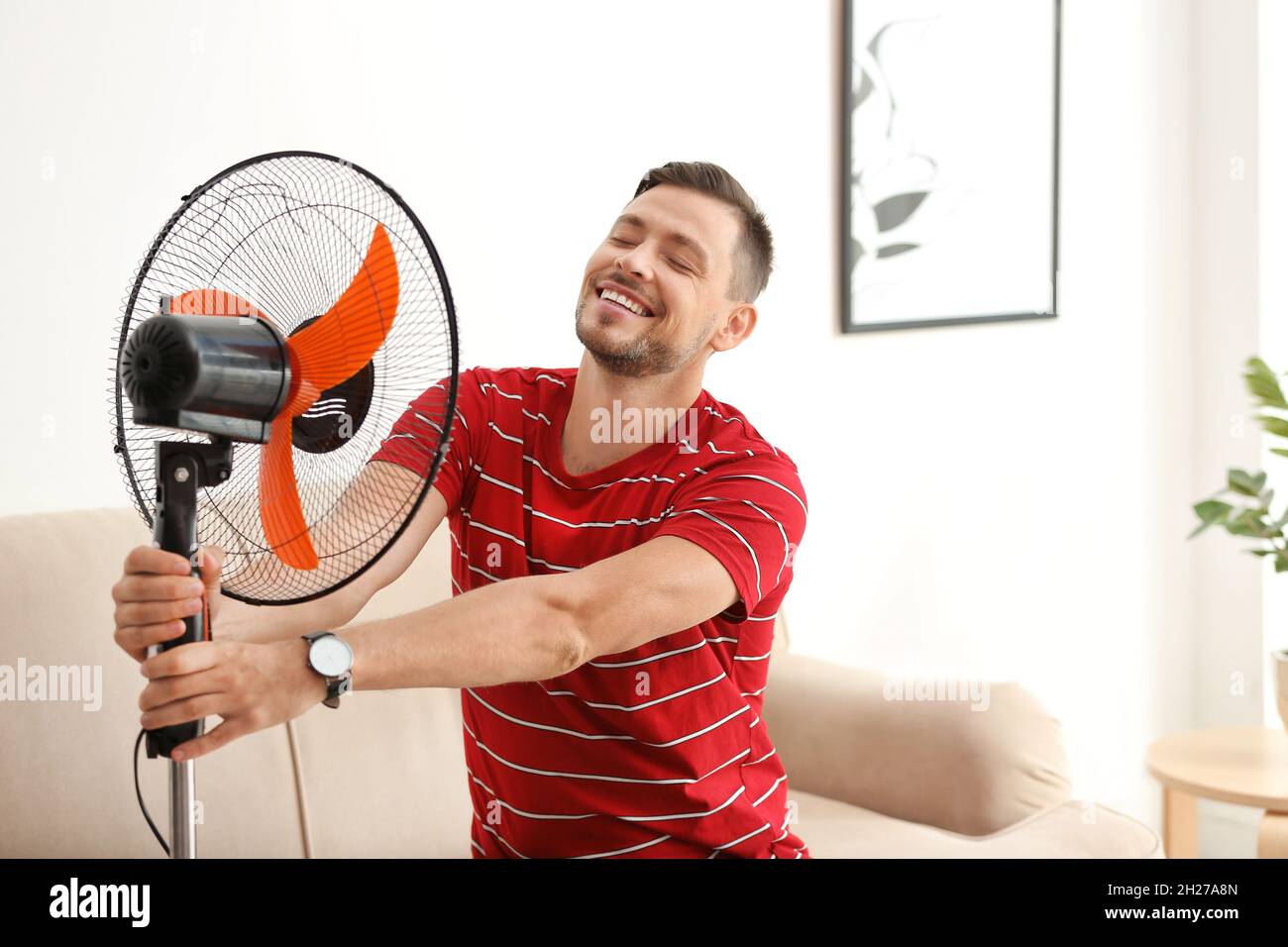 El hombre se refresca del calor delante del ventilador en casa Fotografía de  stock - Alamy