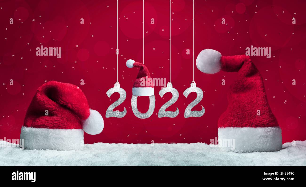 Sombreros de Santa en la nieve sobre fondo rojo, decoración de Navidad. Concepto de vacaciones. 2022. Foto de stock