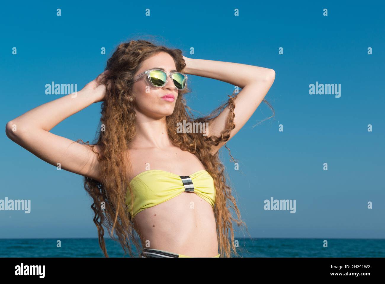 mujer rubia con pelo rizado largo disfrutando del mar adentro primavera o verano Foto de stock