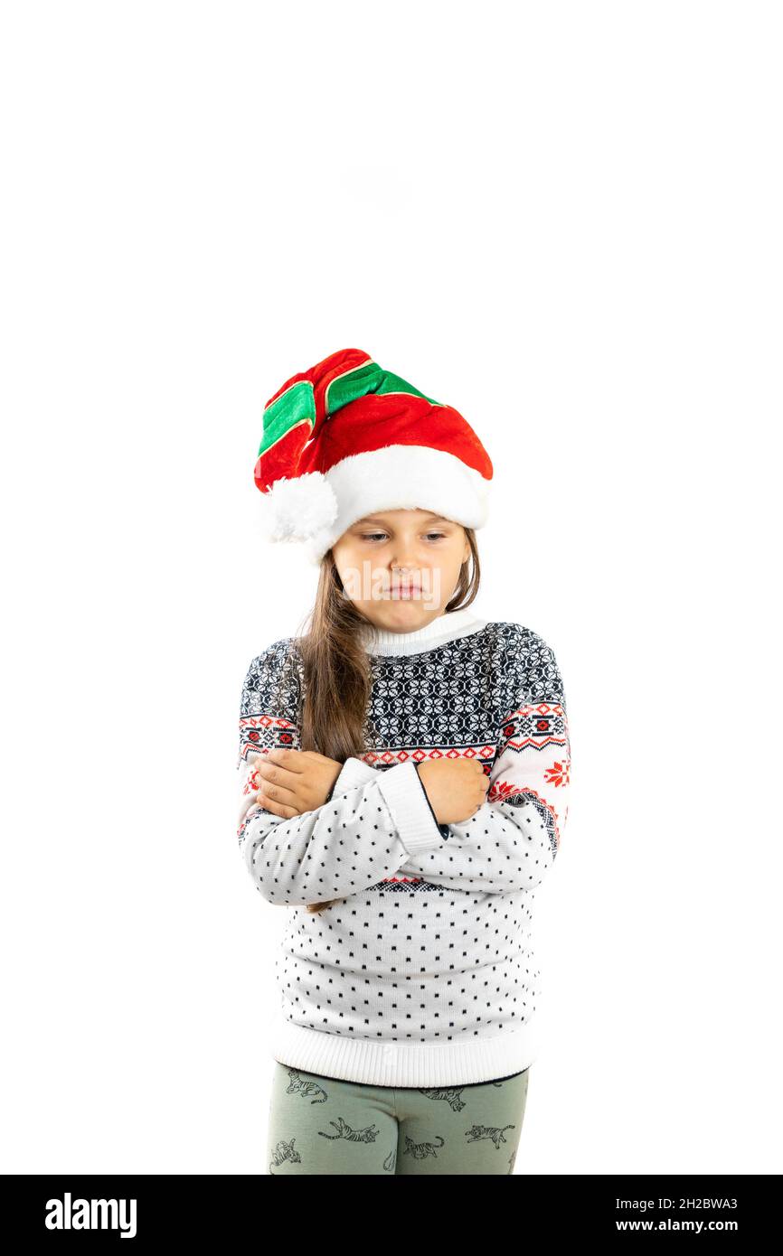 retrato de niña discontenta, desilusionada en jersey de Navidad de punto blanco con reno y sombrero enano con brazos cruzados en el pecho, aislado Foto de stock