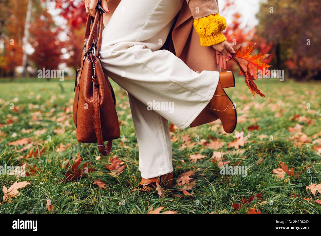Mujer de moda que ropa con estilo accesorios y zapatos caminando en el parque de otoño levantando la pierna. Ropa femenina de otoño. Moderno acampanado, abrigo y Fotografía de stock -