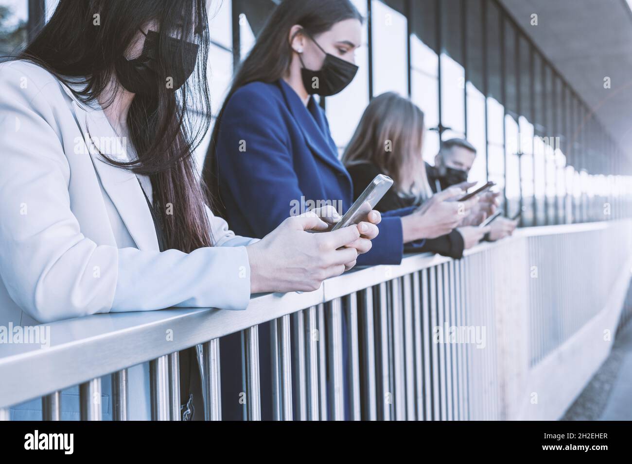 Negocios, distanciamiento social, concepto covid-19. Jóvenes con mascarillas que usan teléfonos celulares en el fondo urbano. Las manos más cercanas de las mujeres están en el campo del pelado Foto de stock