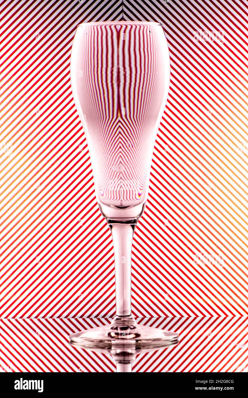 refracción de la luz por una copa de champán tulipán sobre un fondo rojo y blanco a rayas. Arte de vidrio abstracto Foto de stock