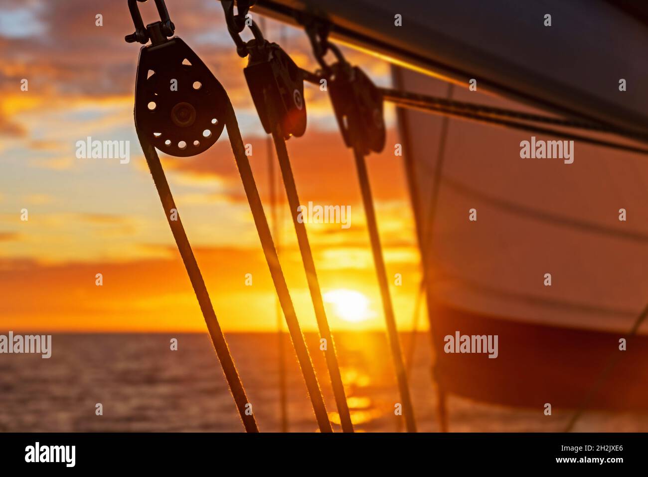 Primer plano de los bloques de barcos de vela / poleas de velero siluetas contra el cielo naranja de la puesta de sol sobre el Mar Caribe Foto de stock