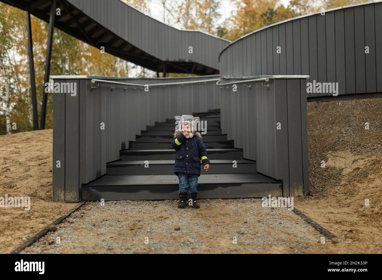 Niño pequeño en sombrero peludo en la parte inferior de la escalera en el bosque Foto de stock