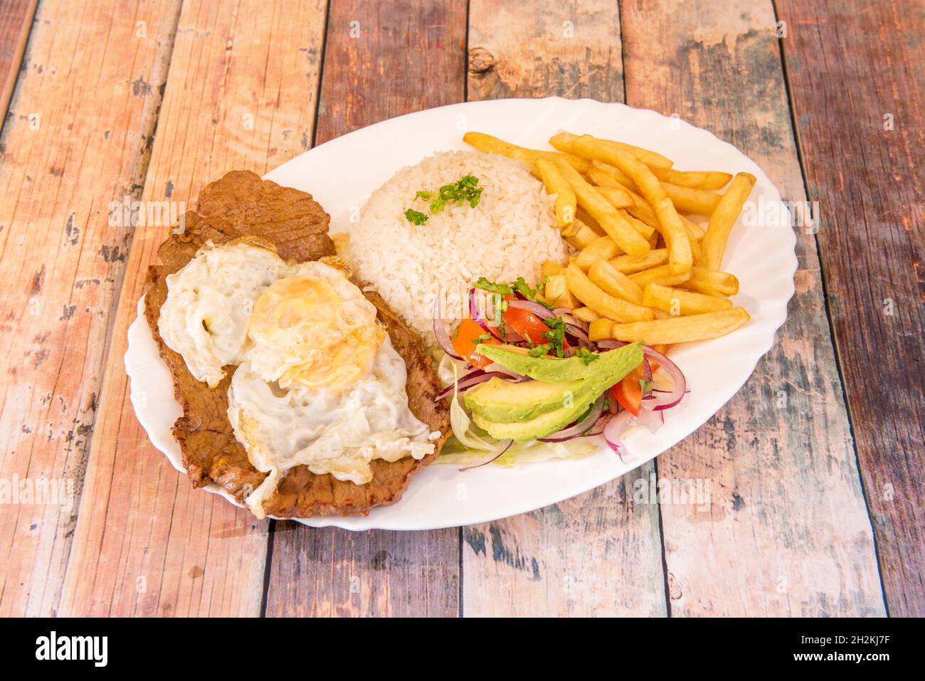 Bandeja de churrasco ecuatoriano con filete de ternera, huevo frito en la  parte superior y varios guarnición de patatas fritas, arroz blanco y  aguacate con ensalada de cebolla púrpura Fotografía de stock -