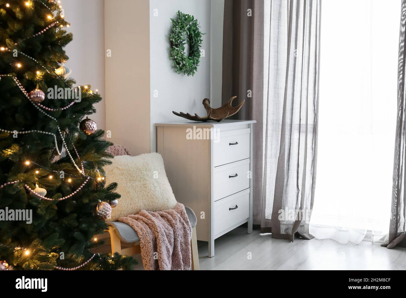 Interior de salón luminoso con árbol de Navidad y corona de muérdago Foto de stock