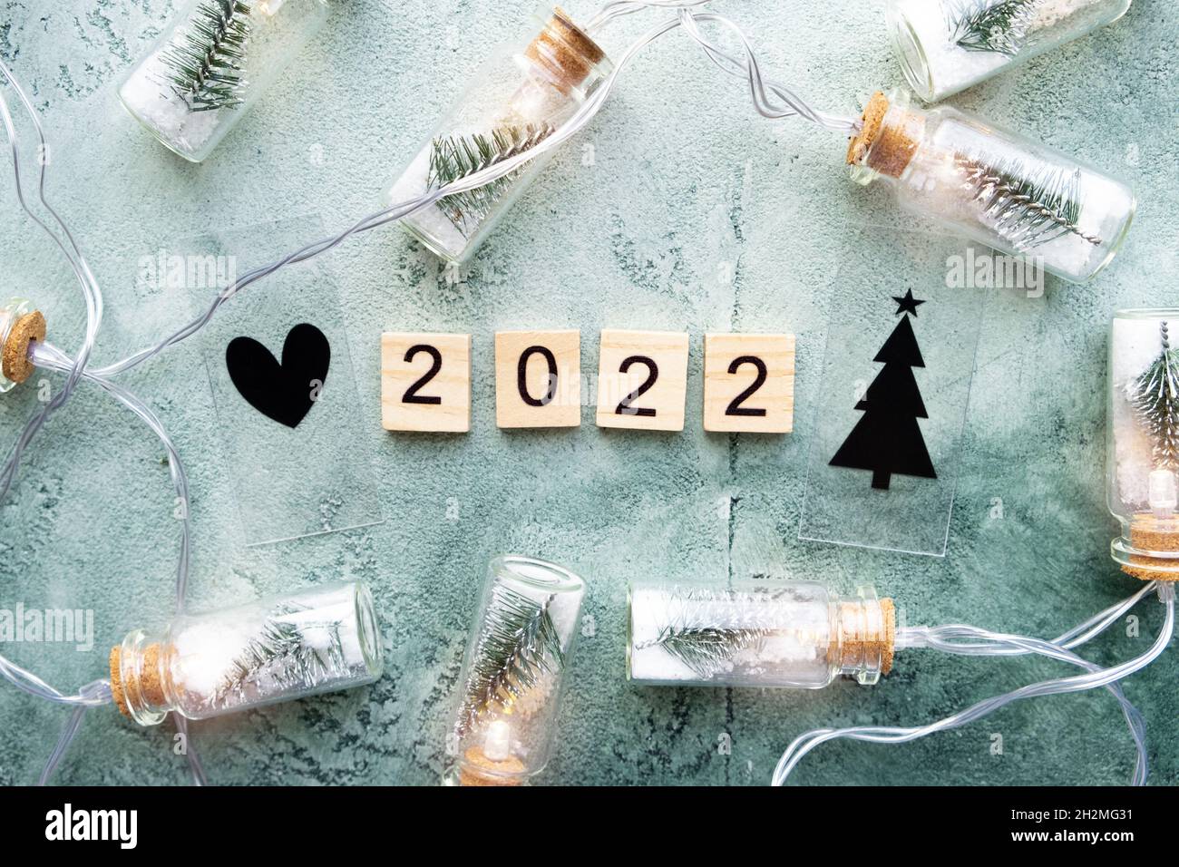 Número 2022 y una brillante guirnalda de jarras de vidrio con árboles de Navidad y nieve en el interior sobre un fondo verde texturizado. Año nuevo y concepto de Navidad Foto de stock