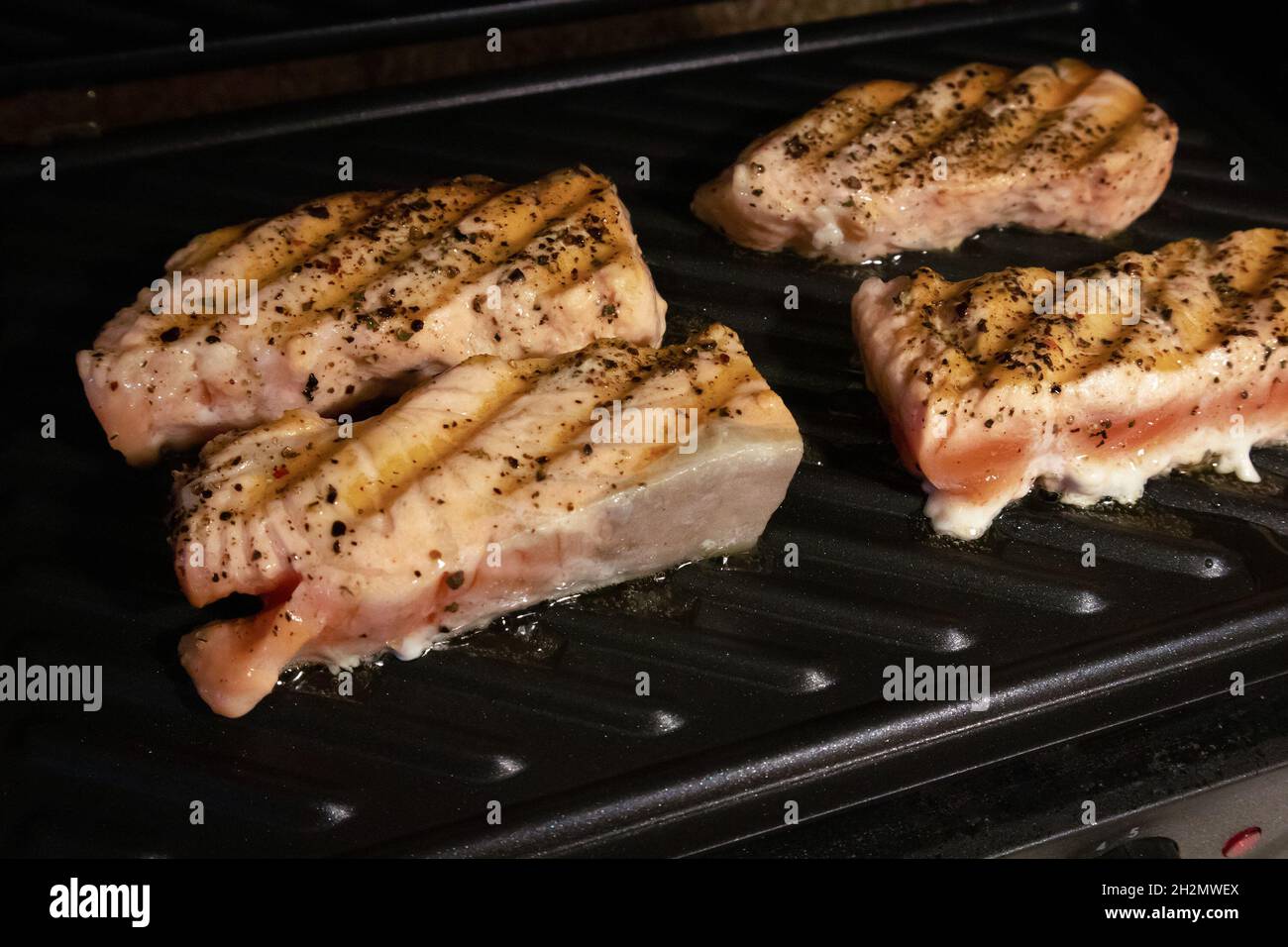 El proceso de freír filetes de salmón en casa en un parrilla eléctrica Foto de stock