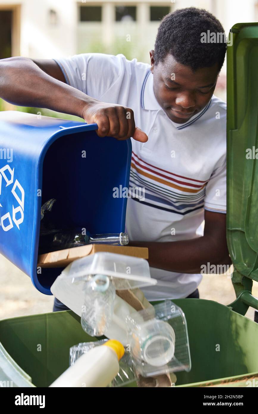Hombre joven Vaciando el Reciclaje de la Casa en un Reciclaje Verde Foto de stock