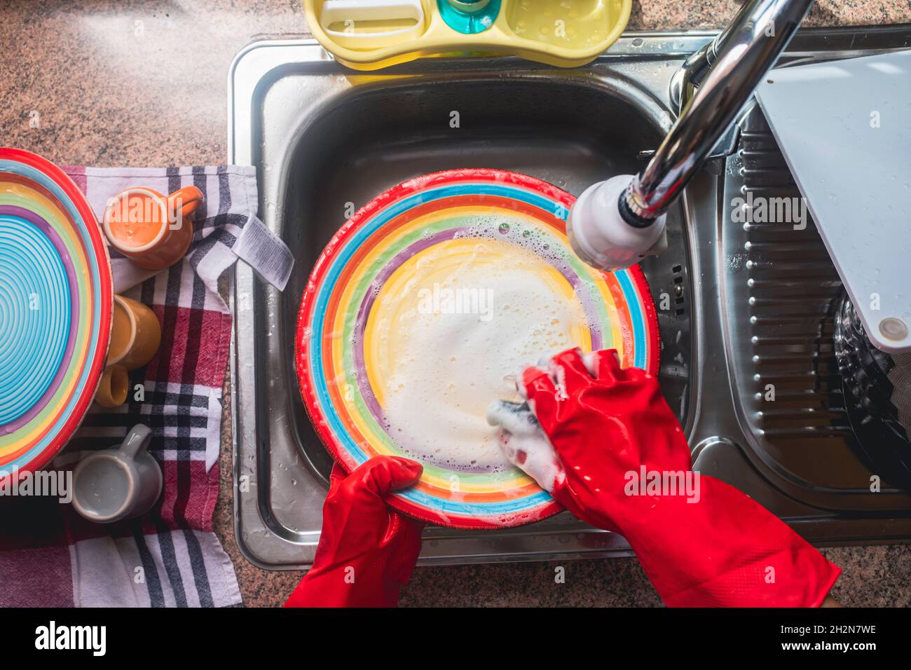 Mujer madura con guantes lavando platos en casa Foto de stock