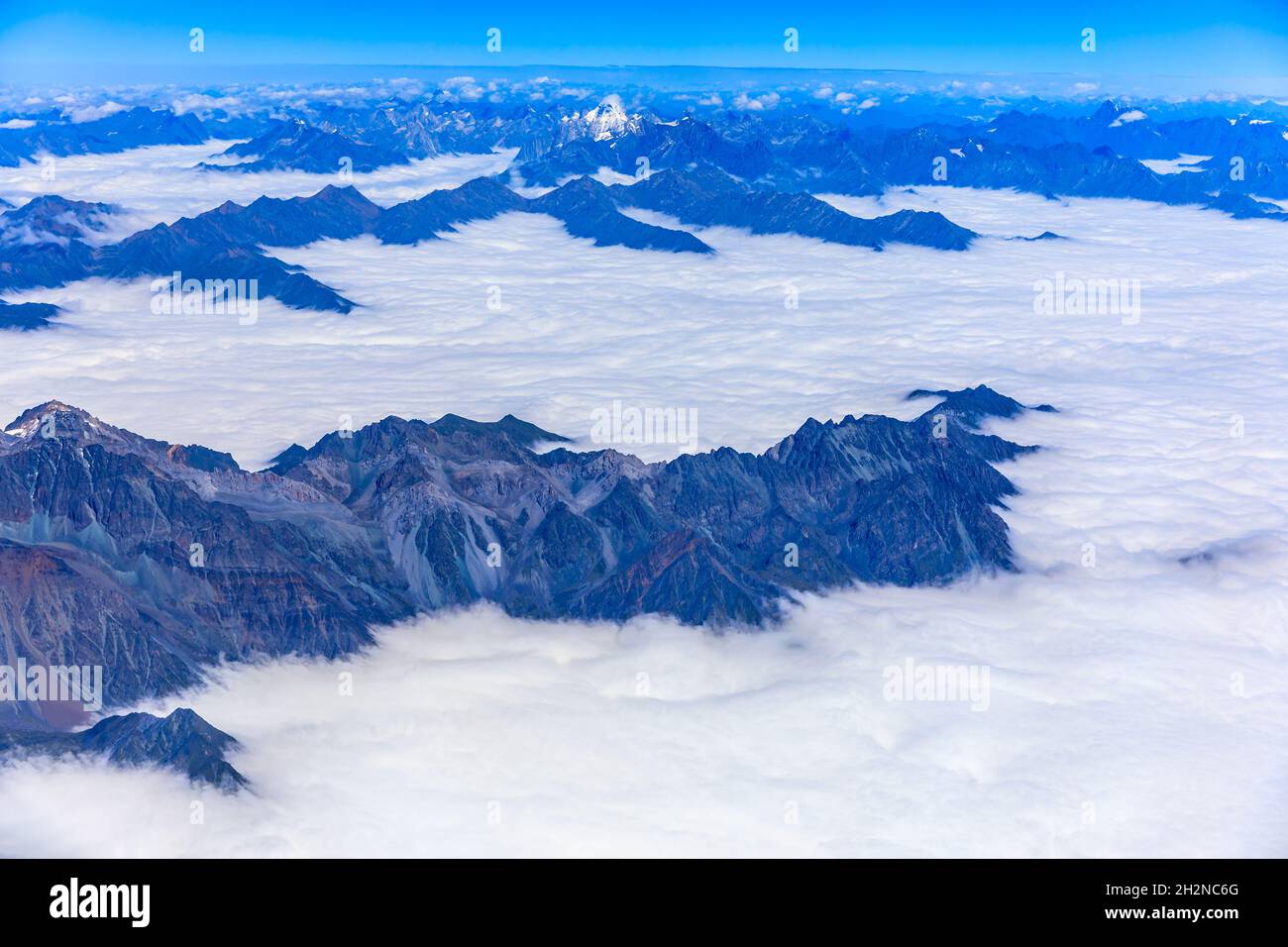 Vista aérea sobre las nubes y picos de montaña en una vista soleada day.mountain desde el avión. Foto de stock