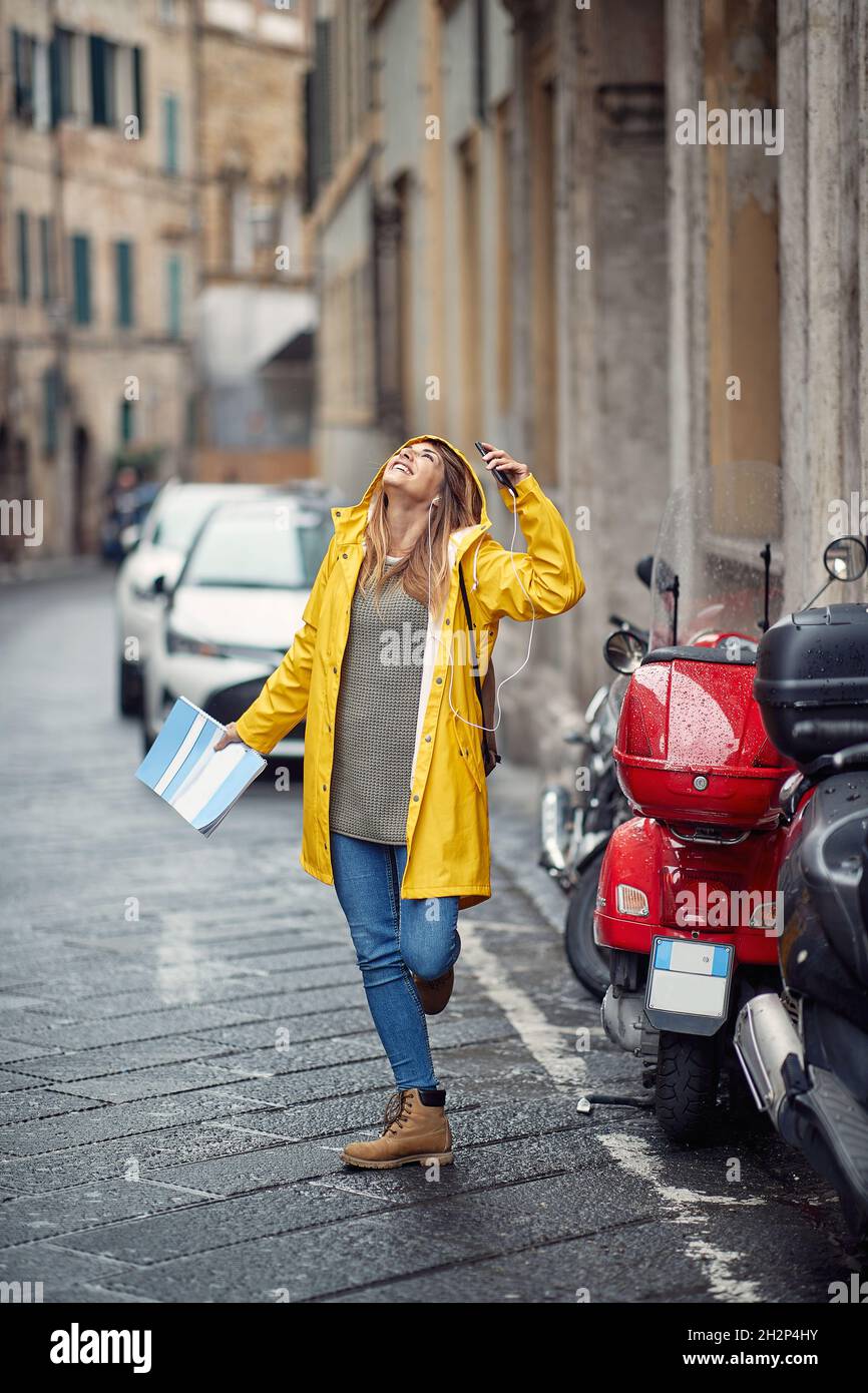 Una mujer sonriente con un chubasquero amarillo escucha música y camina  bajo la lluvia Fotografía de stock - Alamy