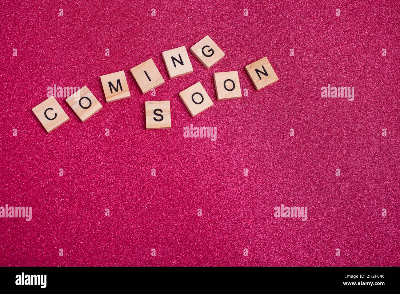 Bloques de madera con texto que viene pronto sobre fondo rosa brillante - copyspace Foto de stock